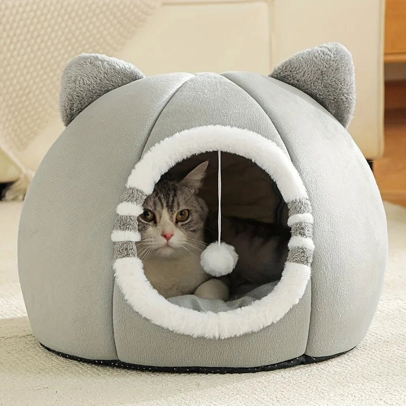Chat tigré installé dans la grotte de couchage grise à oreilles